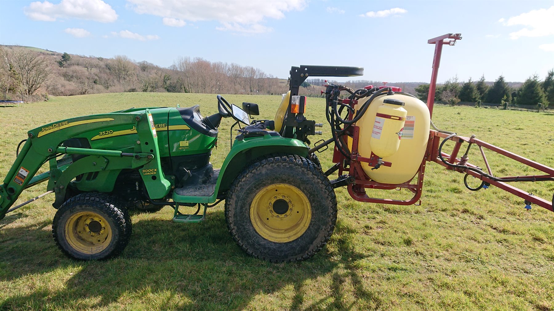 Compact tractor spraying a grassy field