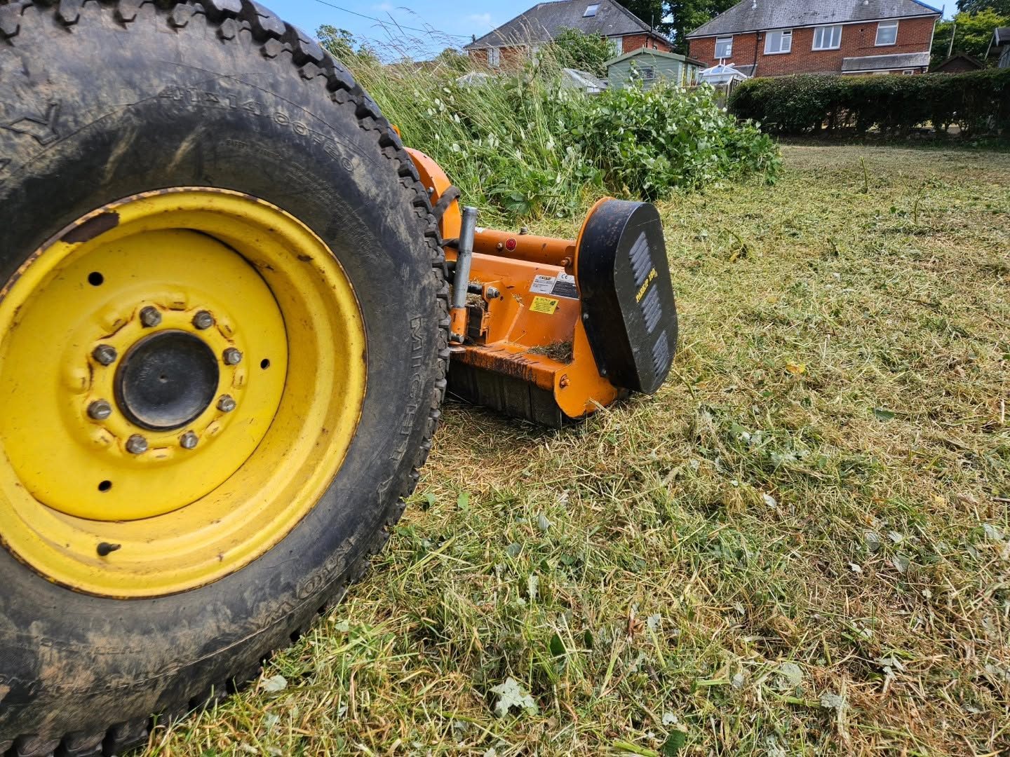 Tractor flail mower cutting long grass on an open site