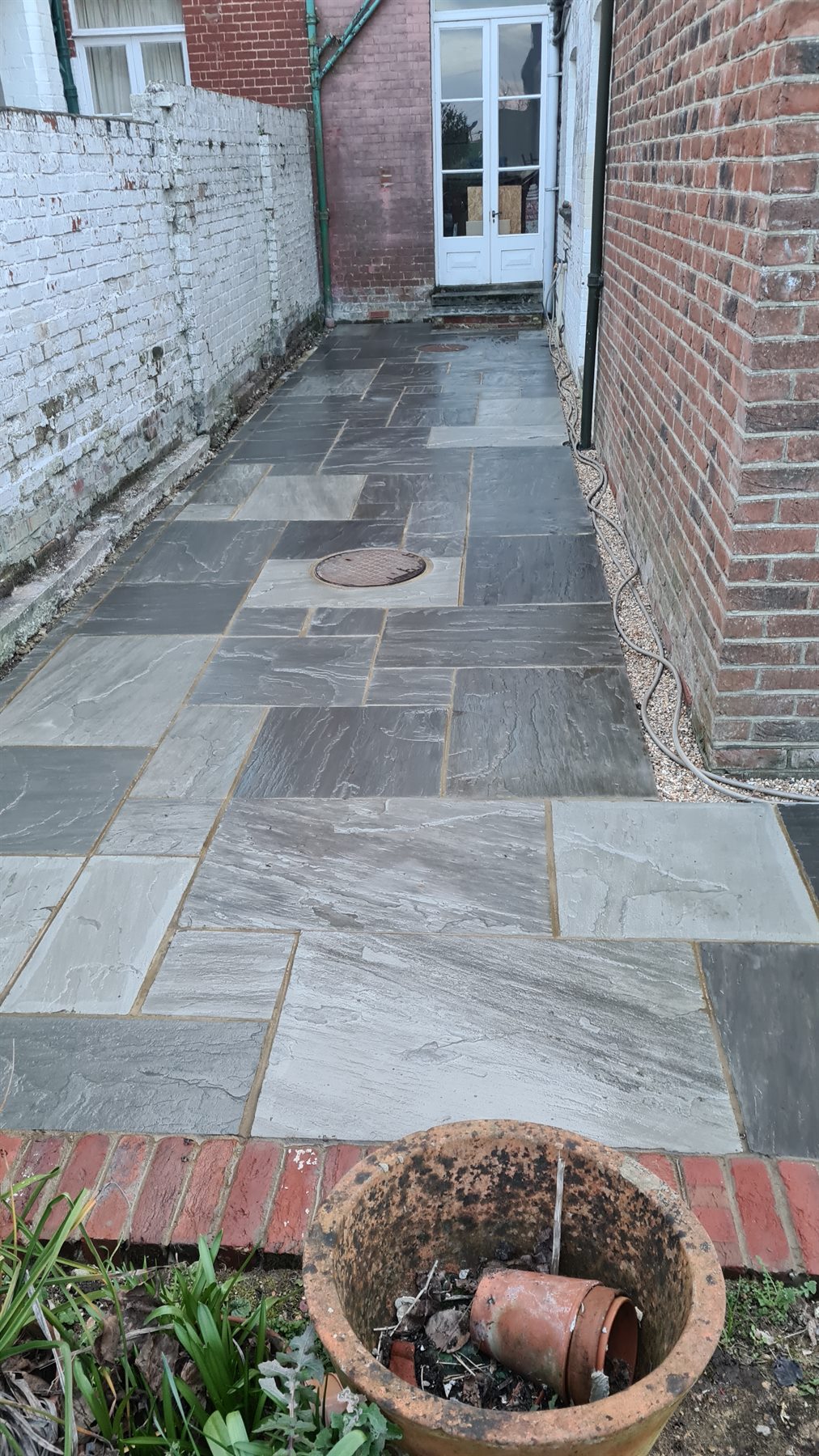 Stone paving being laid along the side of a brick house