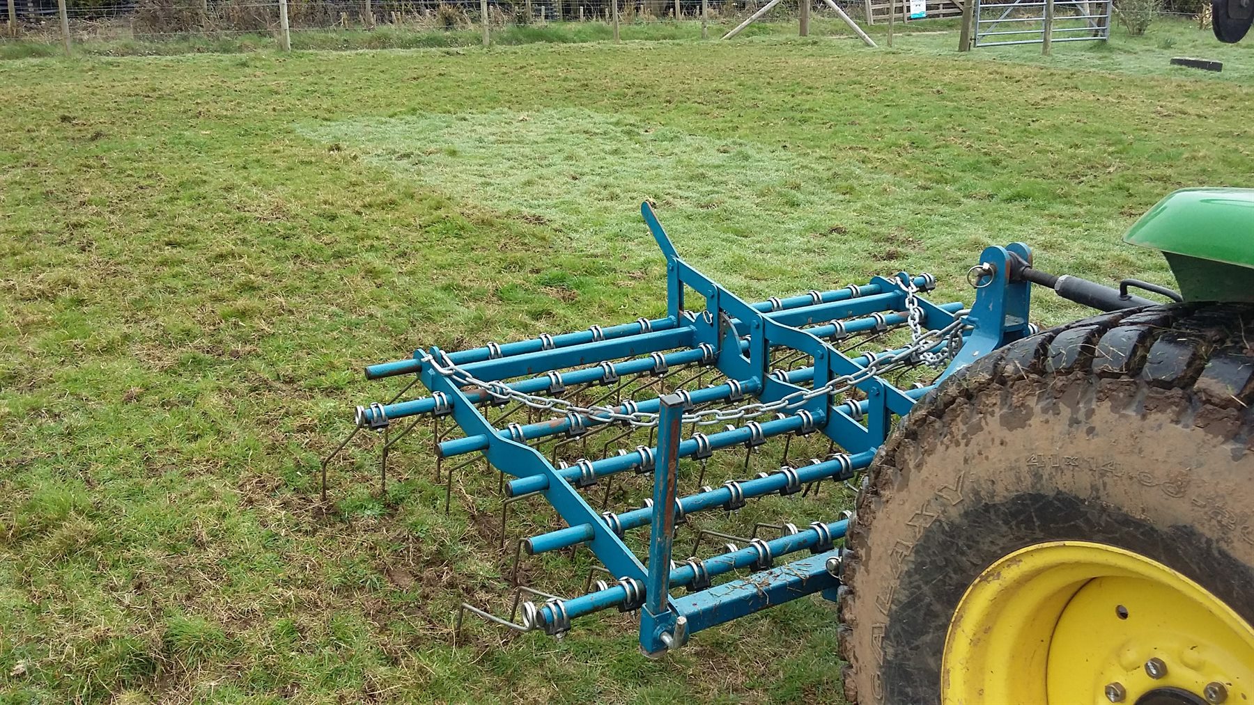 Tractor-mounted harrow working across a paddock
