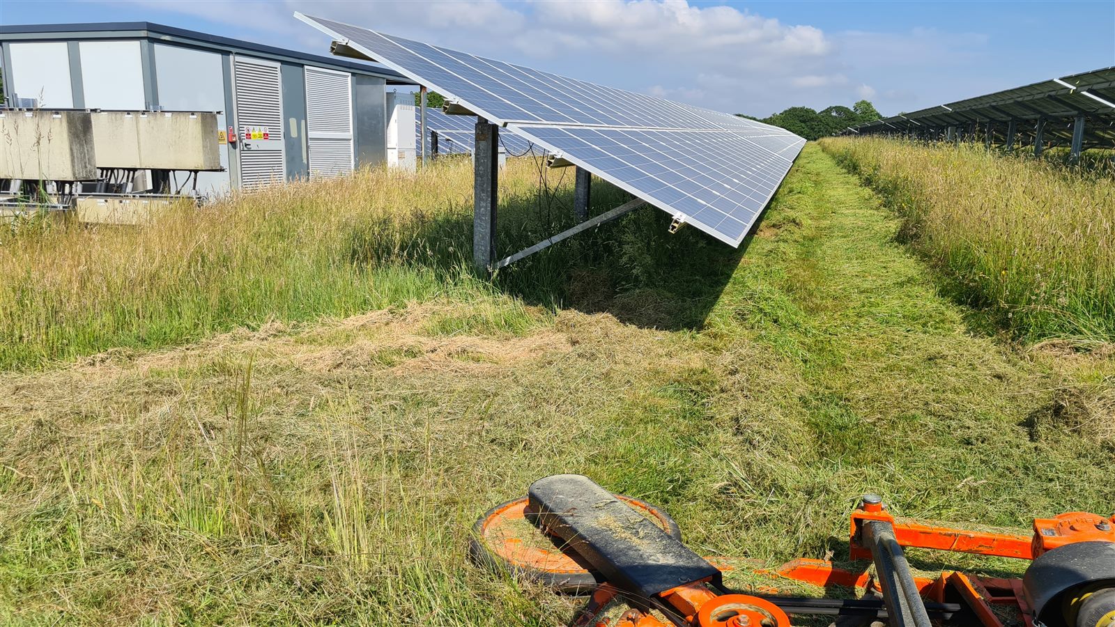 Compact tractor mowing between solar panels